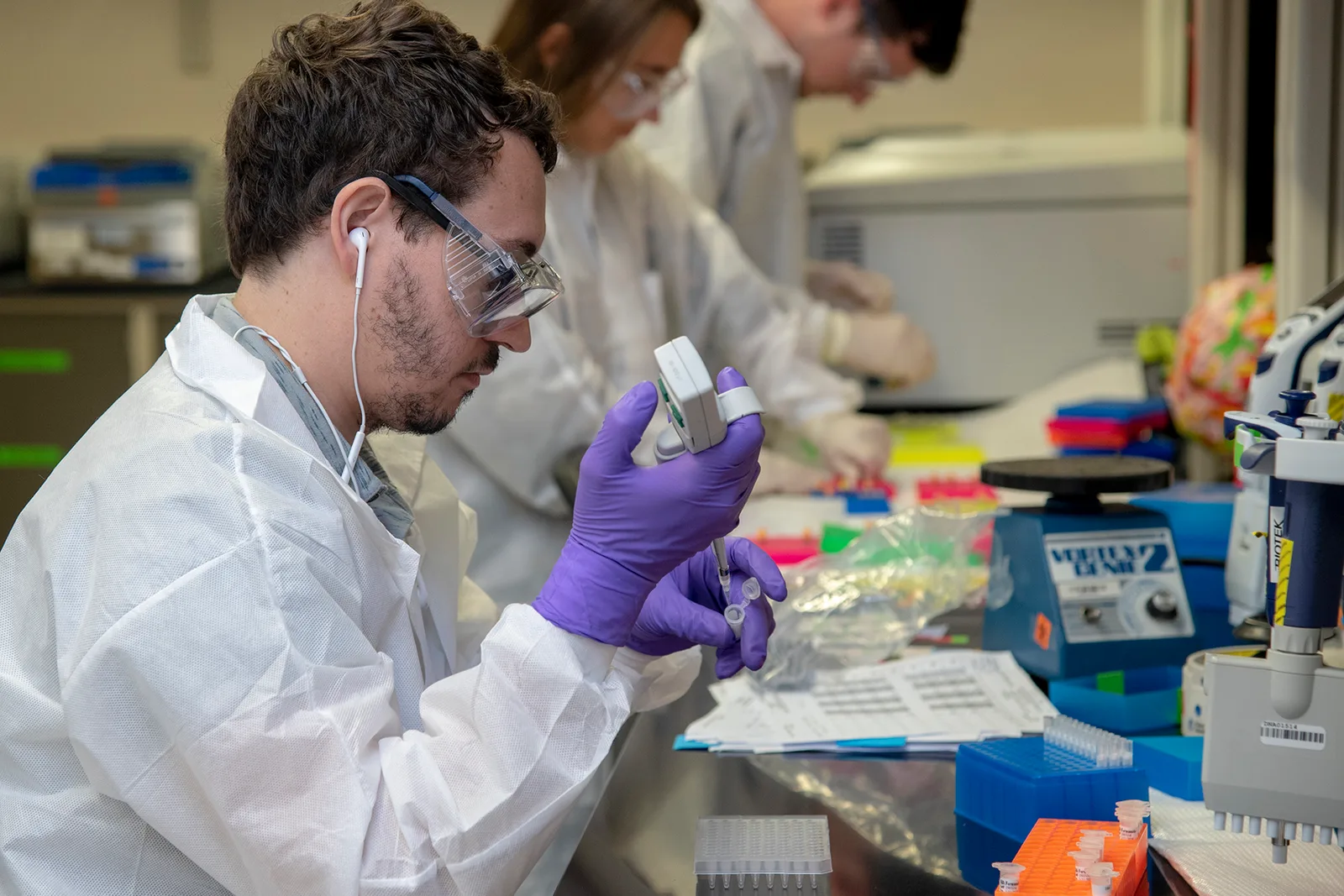 Laboranti v ochranných odevoch a rukaviciach pipetujú vzorky v laboratóriu na identifikáciu DNA
