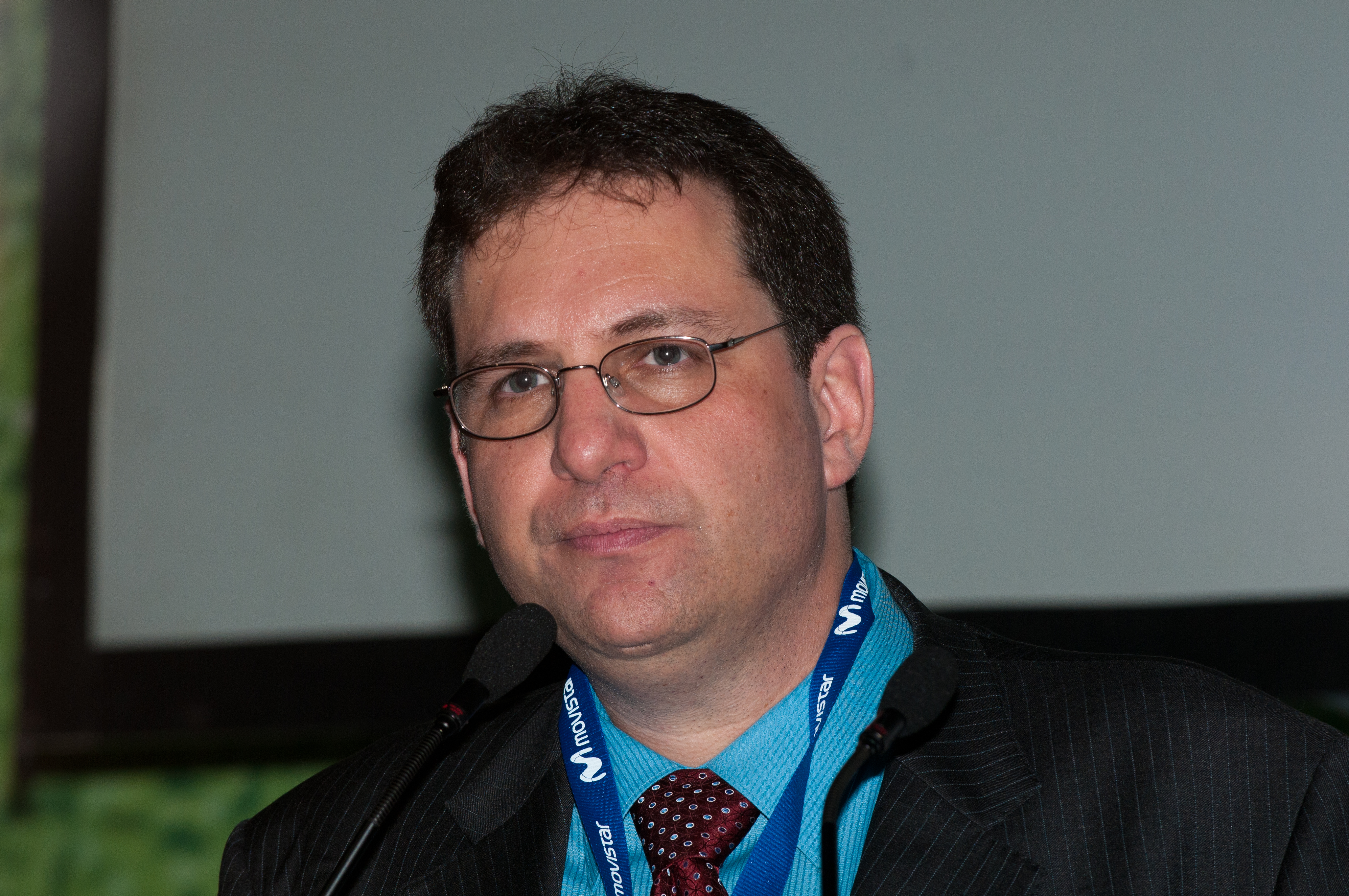 Kevin Mitnick v okuliaroch a saku s visačkou na krku hovorí do mikrofónu na konferencii