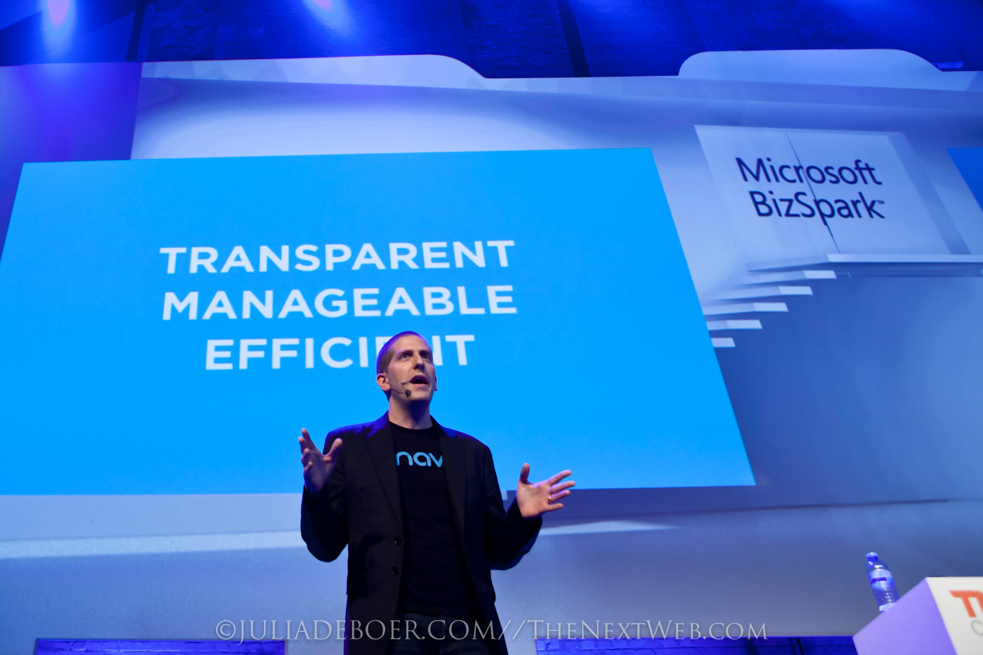 Muž v tričku s logom Onavo prednáša na pódiu pred modrou obrazovkou s nápisom Transparent, Manageable, Efficient