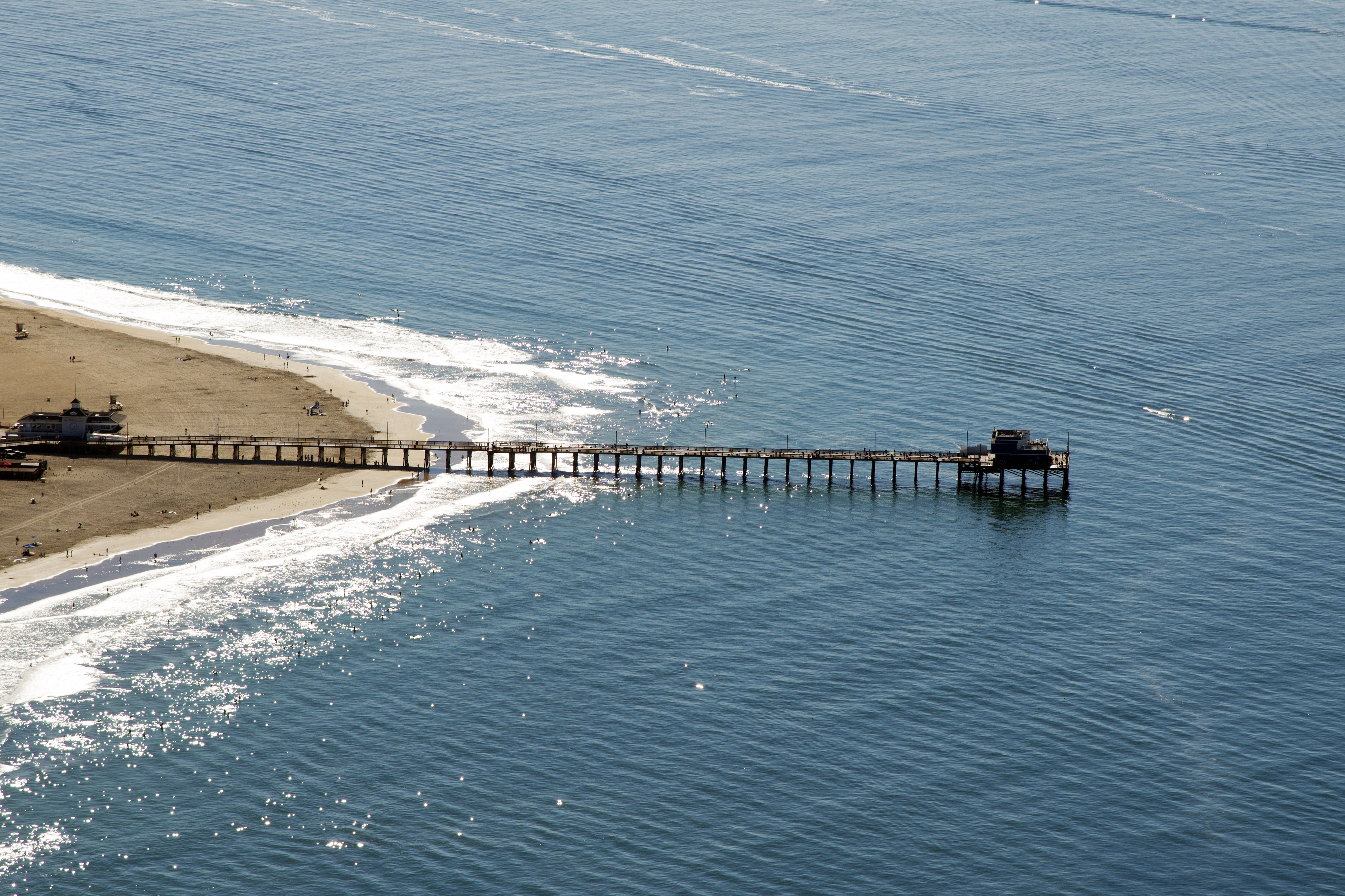Letecký pohľad na piesočnú pláž a dlhé drevené mólo Newport Pier v Tichom oceáne
