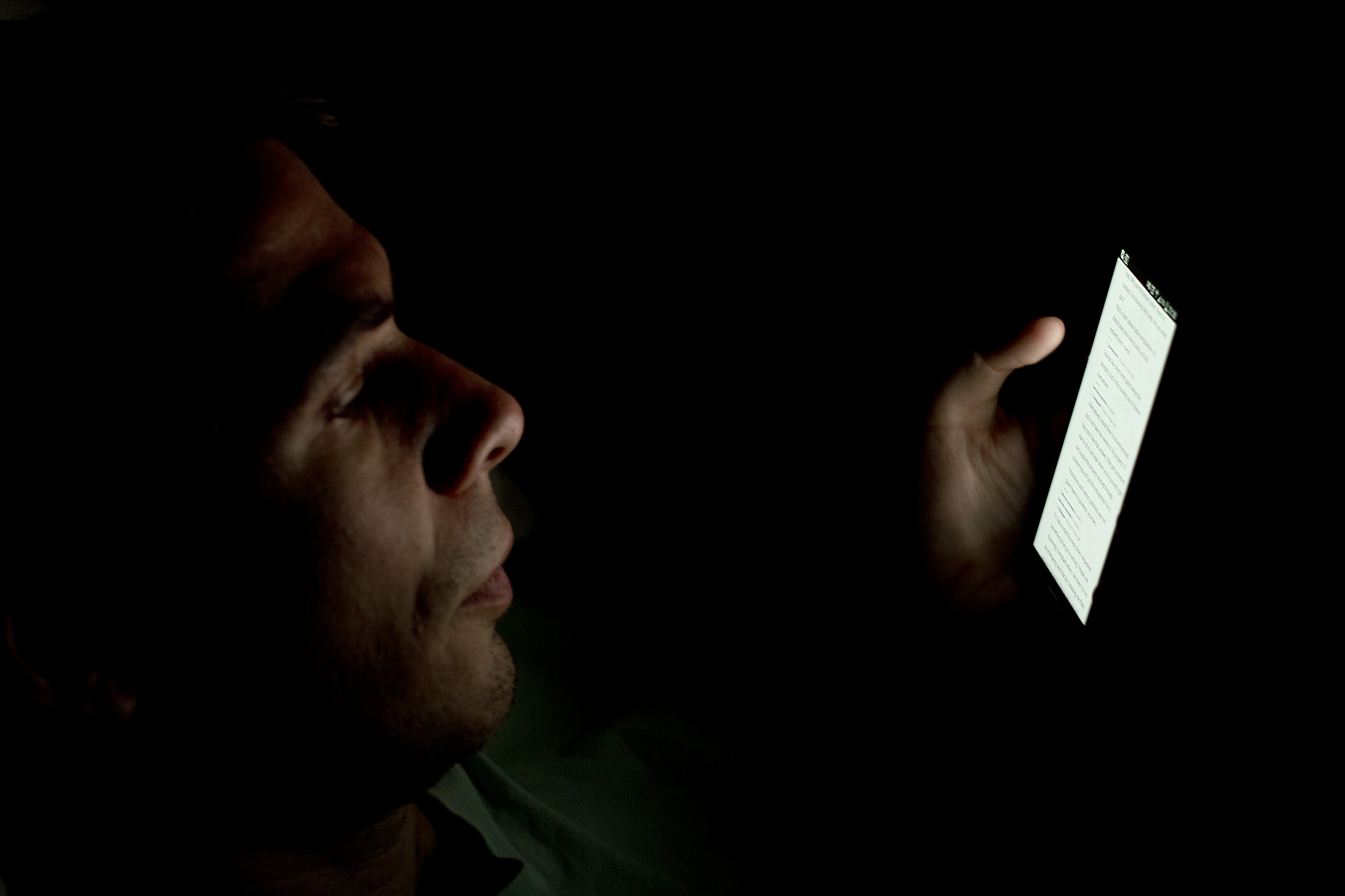 Profil muža v tme osvetlený svetlom z displeja mobilného telefónu, ktorý drží v ruke